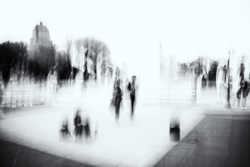 Esplanade très claire, petites silhouettes dispersées, architecture floue, noir et blanc high-key.