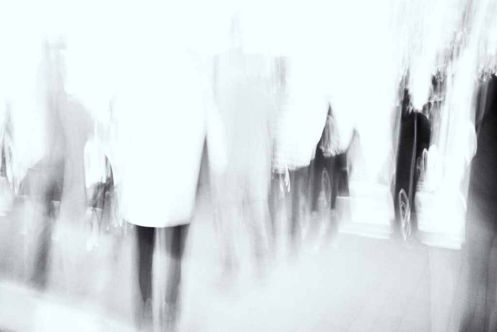Silhouettes proches en mouvement, jambes et manteaux flous, contours adoucis, noir et blanc.
