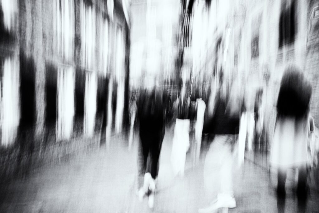 Silhouettes superposées au premier plan, façades verticales, flou ICM, noir et blanc.