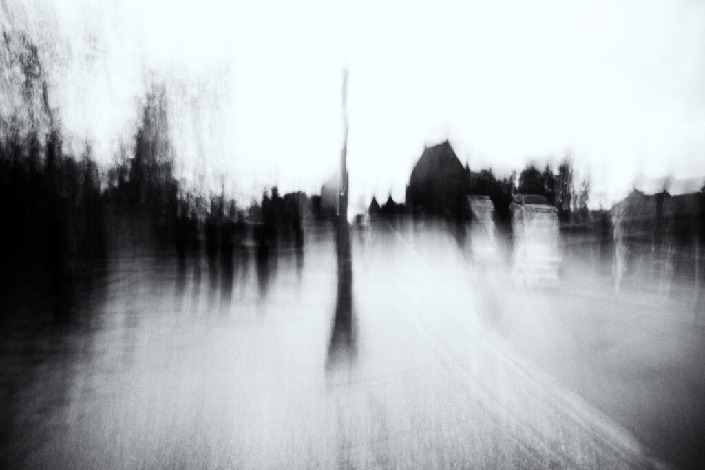 Place urbaine en noir et blanc, silhouettes floues dispersées, bâtiment sombre en arrière-plan.