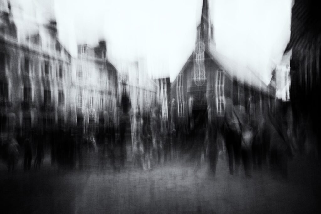 Église et façades urbaines, silhouettes en bas de cadre, flou vertical et latéral en noir et blanc.
